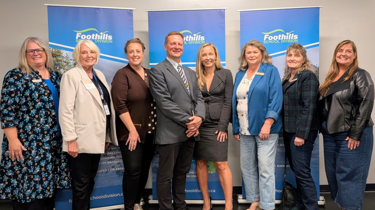 Eight Foothills School Division leaders and partners standing together in front of Foothills School Division banners
