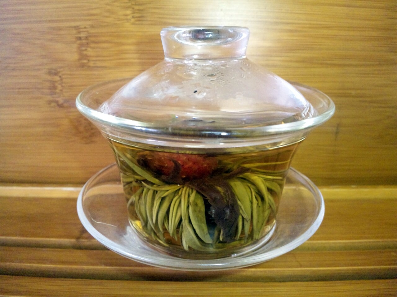 A blooming tea flower unfurling inside a clear glass cup on a wooden table