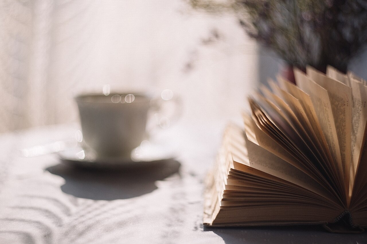 An open book beside a cup of tea on a saucer in soft light