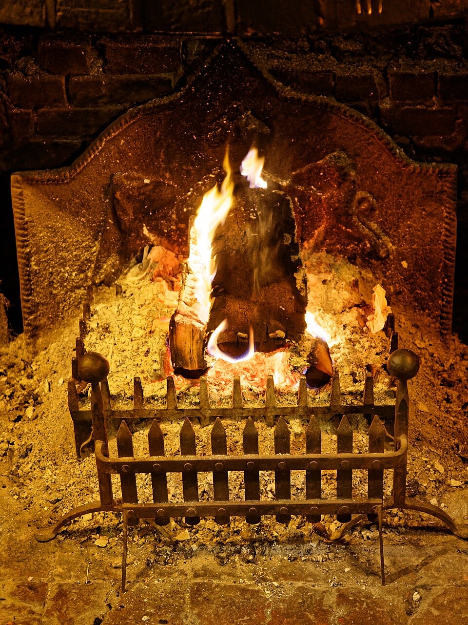 A log fire glowing in an old iron grate in a brick hearth