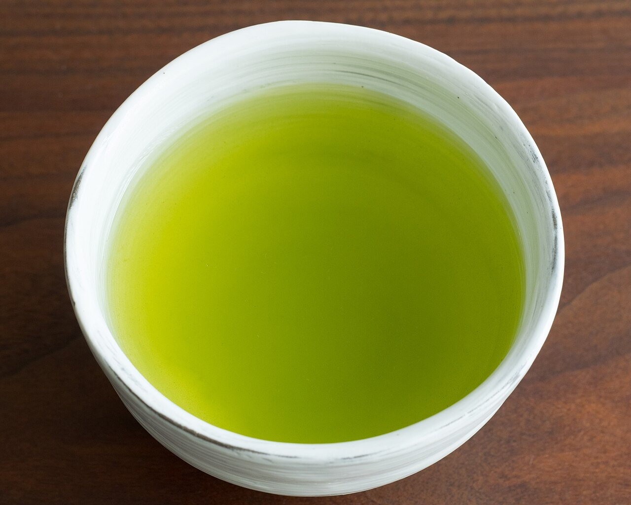 A white cup of bright green Japanese sencha seen from above on a wooden table