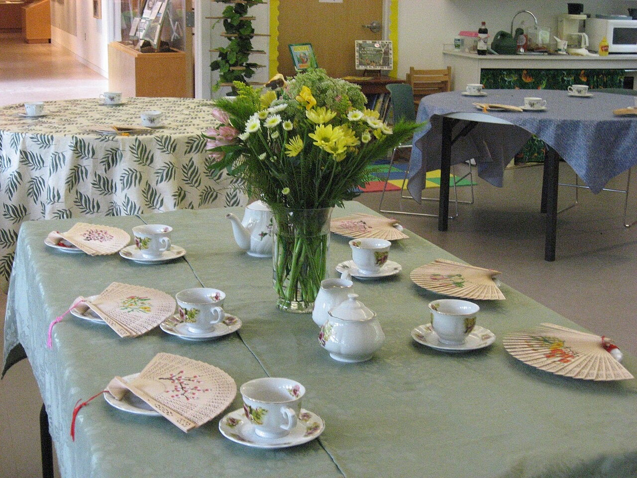 A tea party table laid with a green cloth, flowers, china cups and saucers
